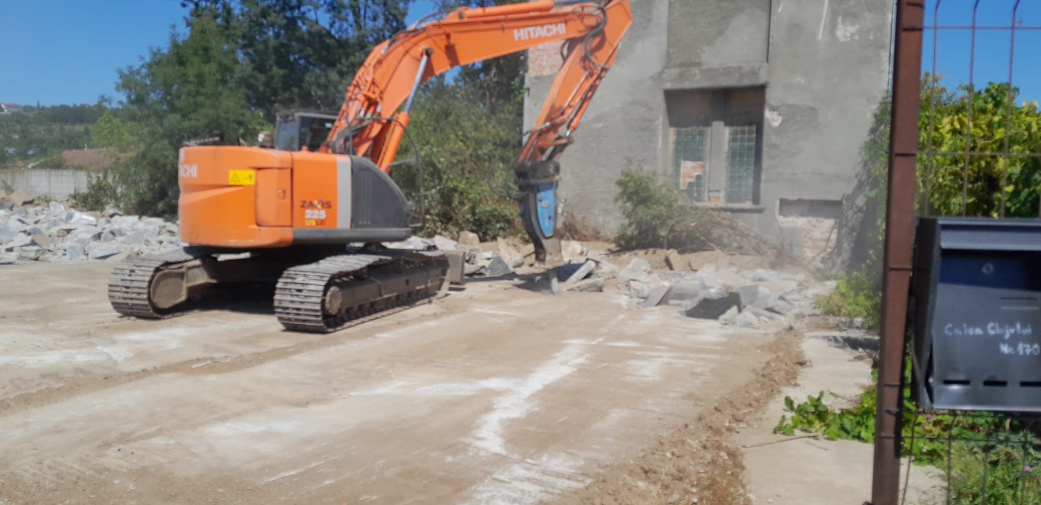Excavator cu ciocan demolator spargand o platforma de beton langa o cladire