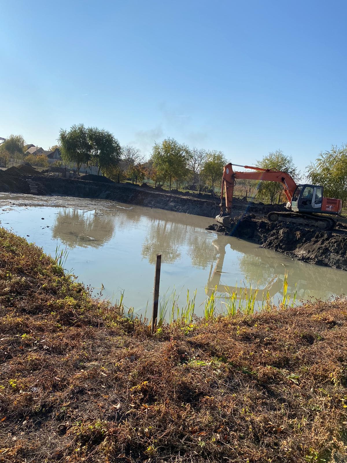 Excavator lucrand pe malul unui iaz in curs de sapare